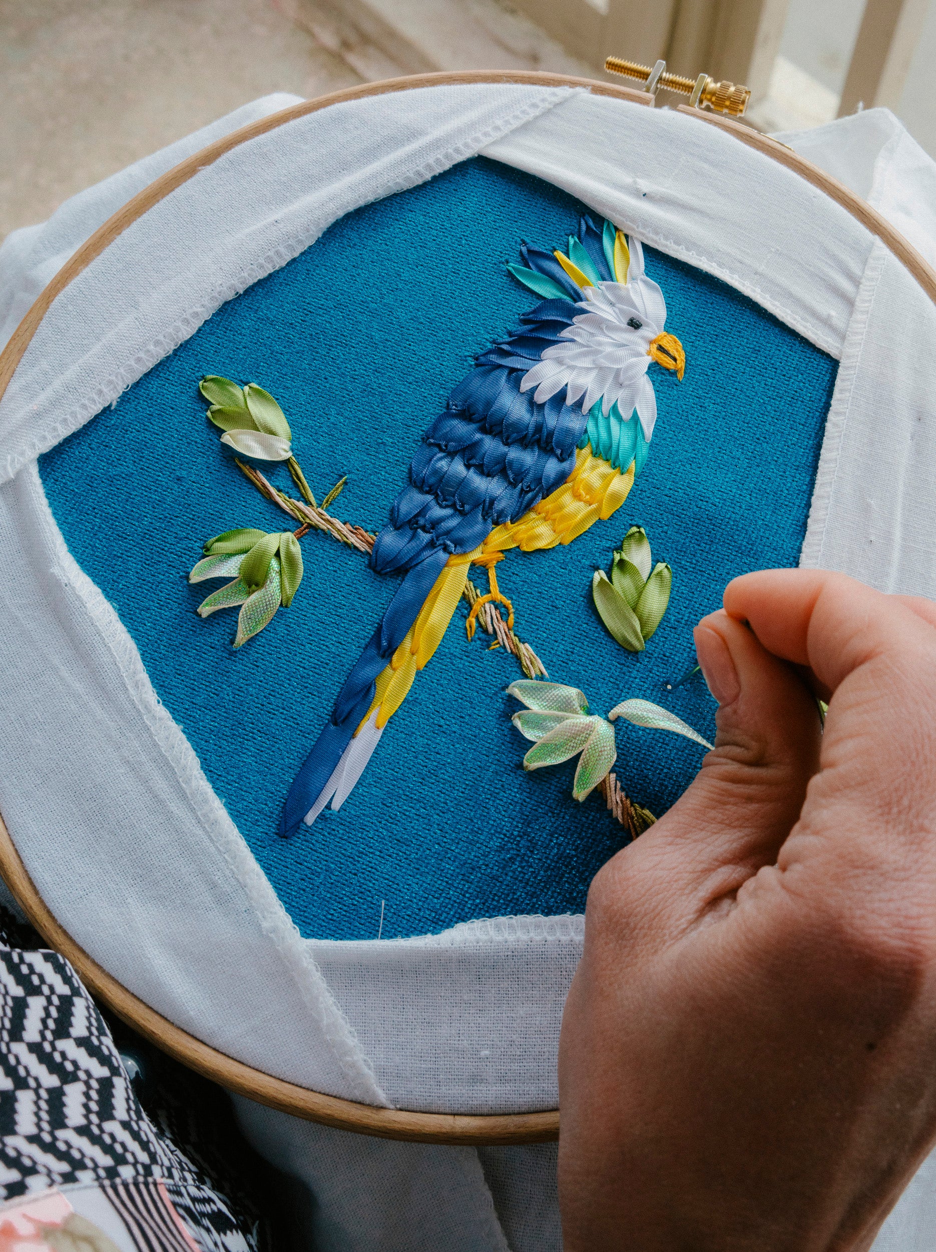 Woman artisan hand-embroidering a bird motif on blue fabric — crafted with patience and artistry by AnatolianCraft.